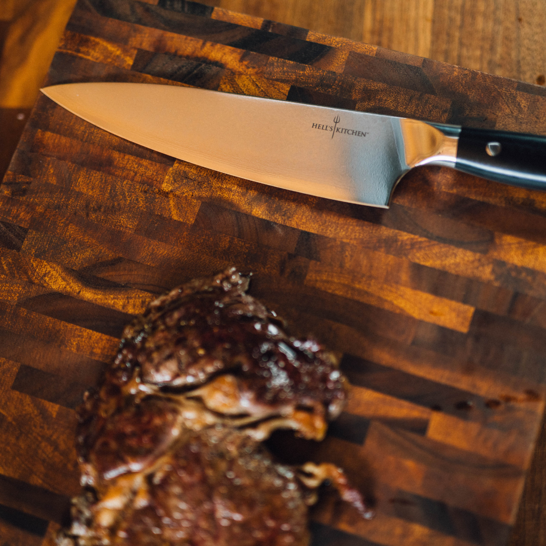 Chef's knife on a wooden cutting board with a piece of roasted meat